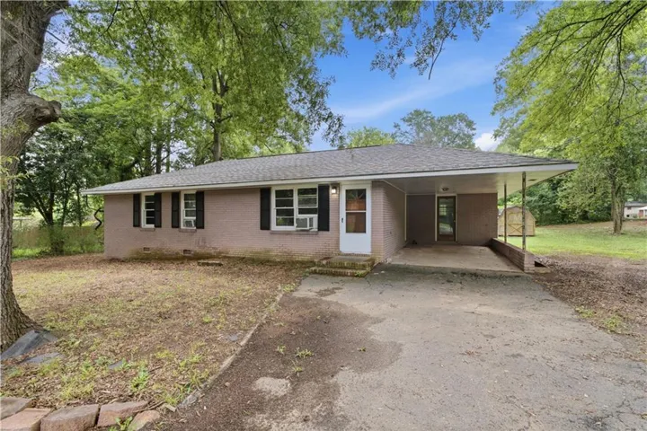 Brick ranch-style exterior featuring a covered carport, dark shingle roof, and white-trimmed windows with dark shutters