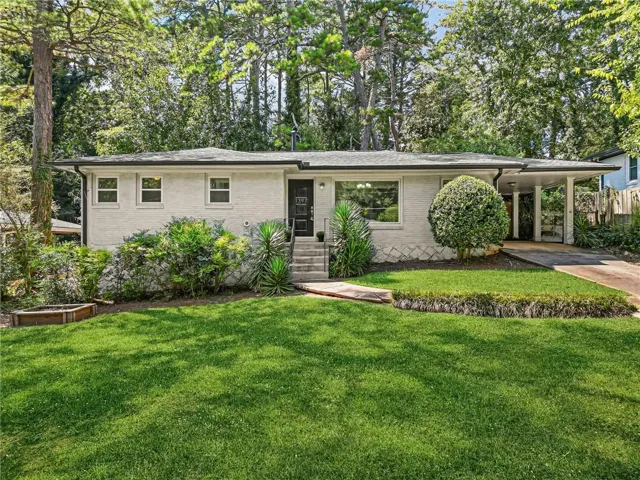 Single-story residence featuring a painted brick exterior, covered carport, front entry porch, mature landscaping, and a manicured lawn