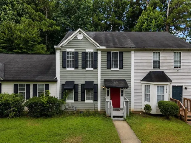 Green siding with white trim, black window shutters, a red entry door, a bay window, and a concrete walkway