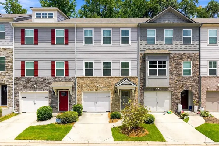 Multi-level townhome with stone veneer and horizontal siding facade, multiple windows, attached garage, and covered entryway