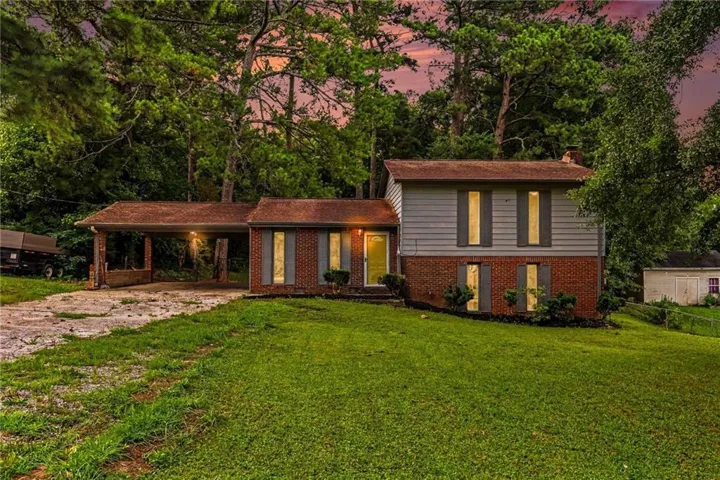 Split-level residence featuring brick and siding exterior, a covered carport, and a prominent front lawn