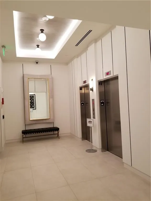 Hallway with a raised ceiling, elevator, and light tile patterned floors
