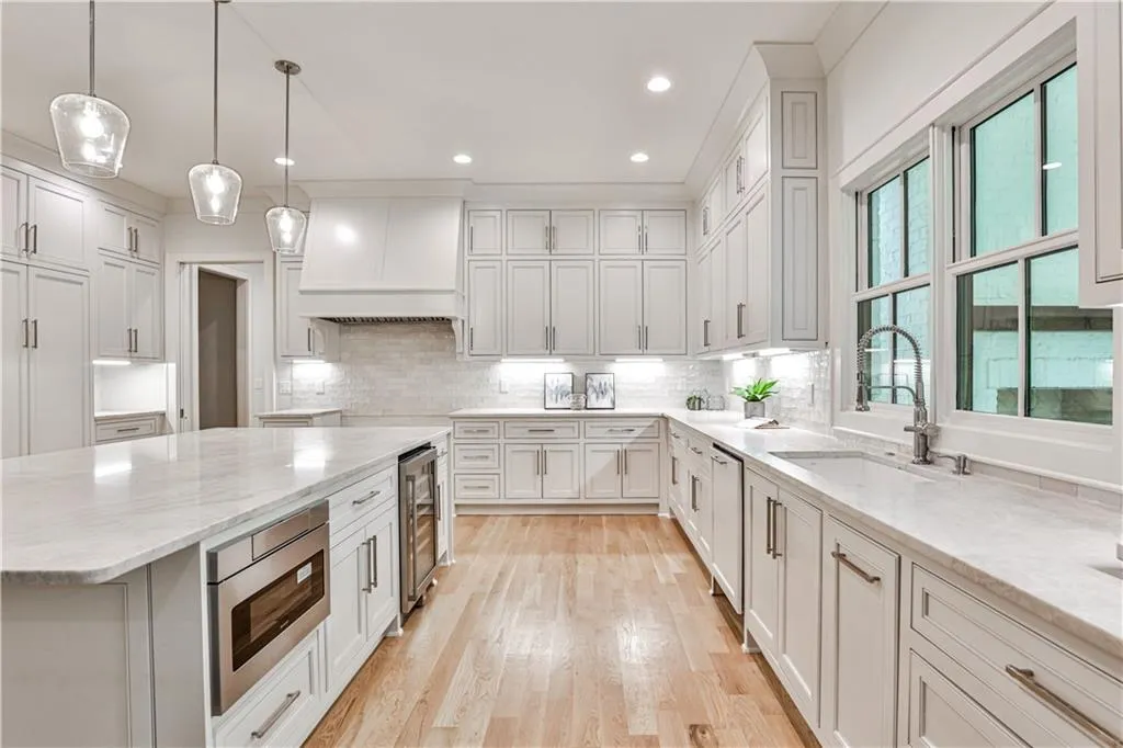 Kitchen featuring premium range hood, light hardwood / wood-style flooring, backsplash, light stone counters, and sink