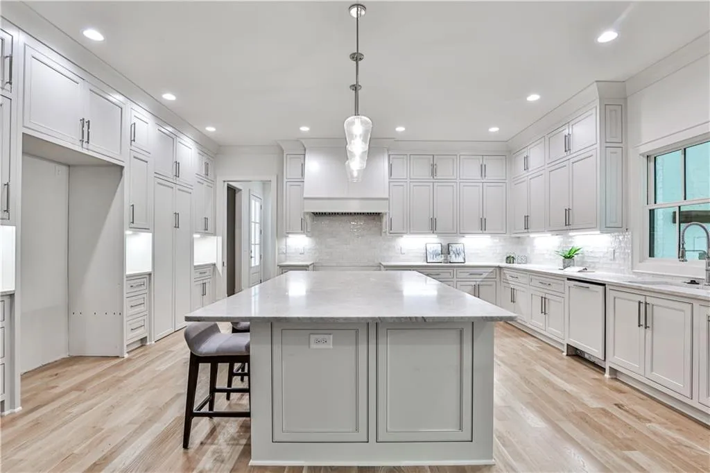 Kitchen with backsplash, hanging light fixtures, light hardwood / wood-style floors, sink, and a center island