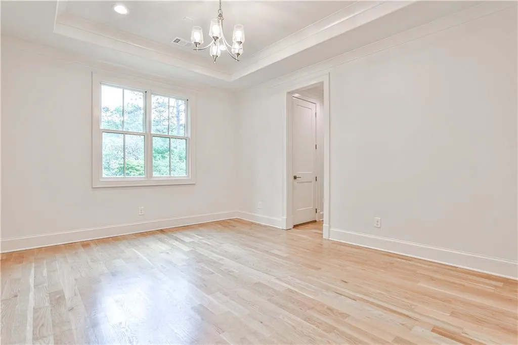 Empty room featuring a raised ceiling, light wood-type flooring, and a chandelier