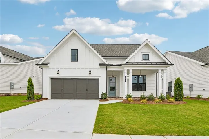 Modern farmhouse exterior featuring white board and batten siding, a covered entry porch with decorative columns, a two-car garage with dark wood-look doors, a light blue entry door, and a concrete driveway