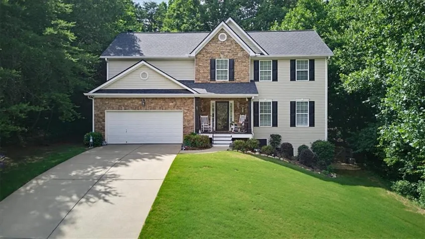 Two-story residence featuring a stone and siding facade, a two-car garage, and a covered front porch