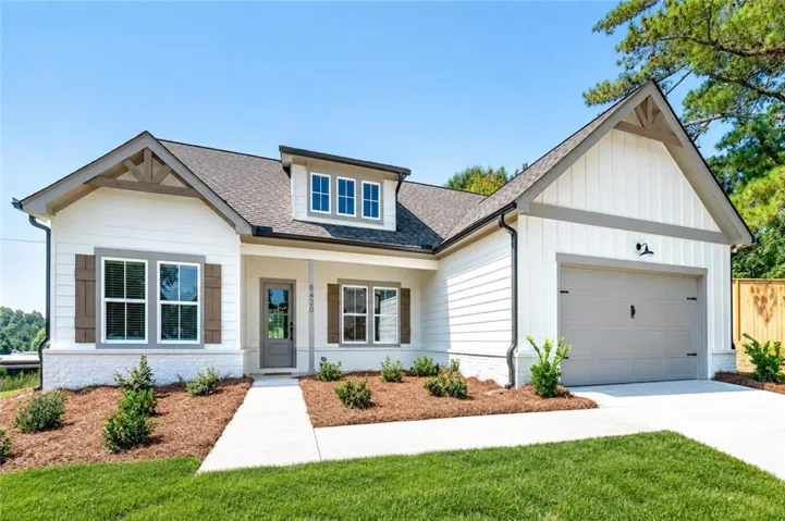 White siding exterior with a grey garage door, covered entry, front landscaping, and a concrete driveway