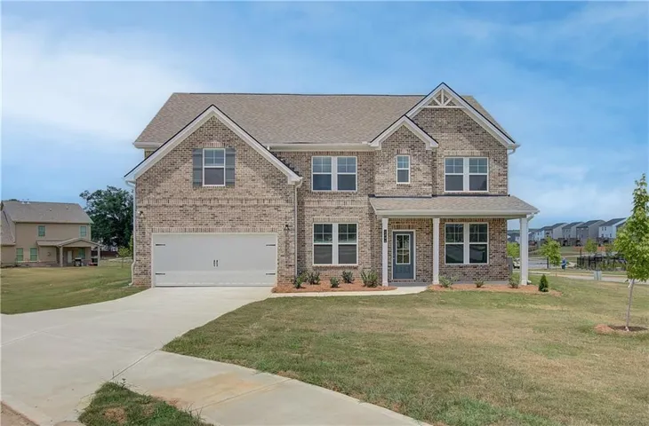 Two-story brick facade residence featuring a covered front porch, an attached two-car garage, multiple gables, and a concrete driveway