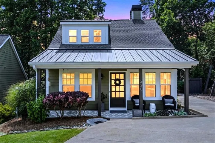 Cottage-style exterior featuring a broad front porch, a dormer with three windows, a gray shingle roof, and a contrasting metal awning