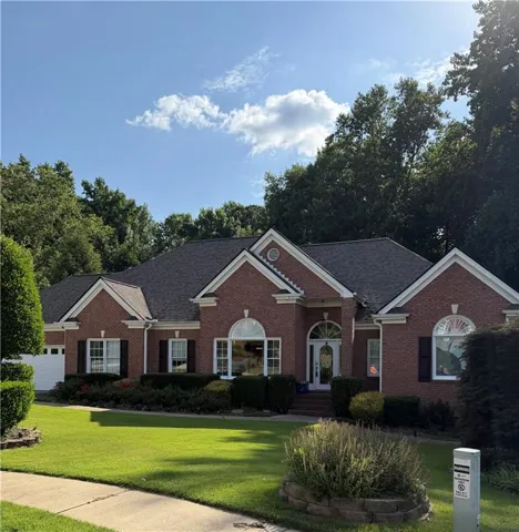 Brick-clad exterior with a dark shingle roof, featuring a manicured lawn, established shrubs, and an arched entry door