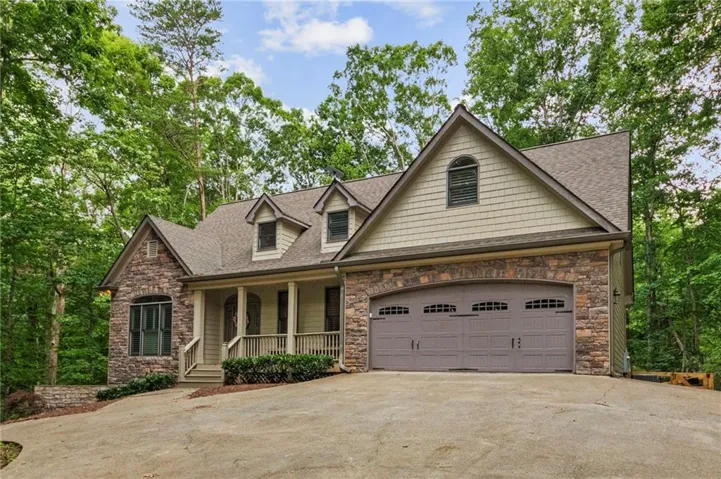 Stone and shake siding exterior with dormer windows, covered front porch, and an attached two-car garage