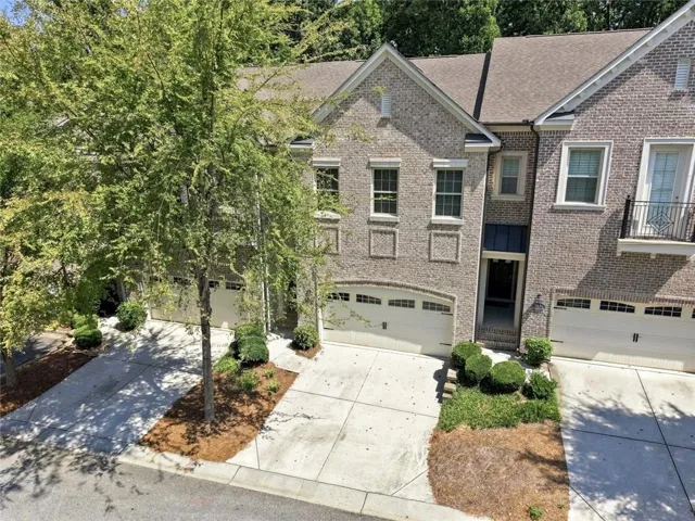 Brick exterior with multiple windows, two-car garage, and mature landscaping