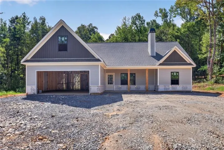 Siding exterior with a covered porch, an attached garage, a prominent chimney, and a gravel driveway