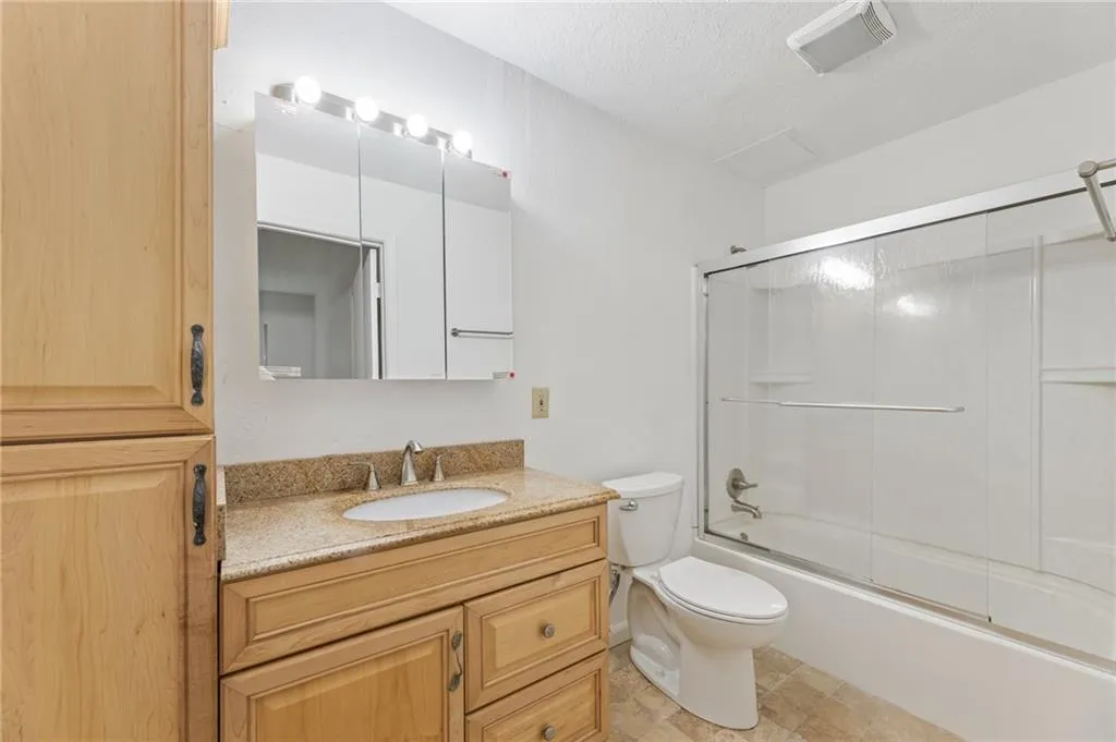 Full bathroom featuring a textured ceiling, tile patterned flooring, vanity, bath / shower combo with glass door, and toilet Full bathroom featuring a textured ceiling, tile patterned flooring, vanity, bath / shower combo with glass door, and toilet