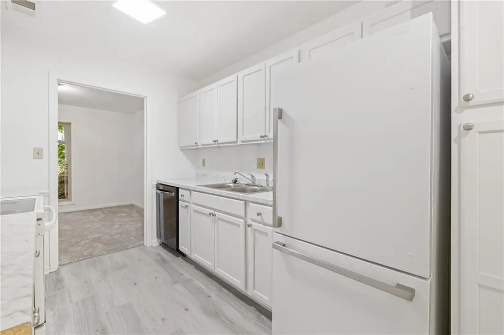 Kitchen featuring sink, white refrigerator, light wood-type flooring, stainless steel dishwasher, and white cabinetry Kitchen featuring sink, white refrigerator, light wood-type flooring, stainless steel dishwasher, and white cabinetry