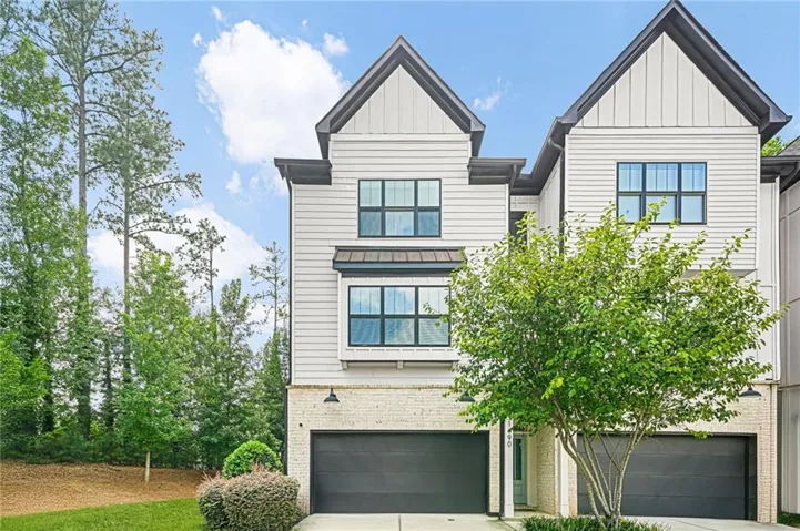 Modern townhome exterior featuring light-colored siding, dark trim, black-framed windows, a two-car garage, and a brick lower facade