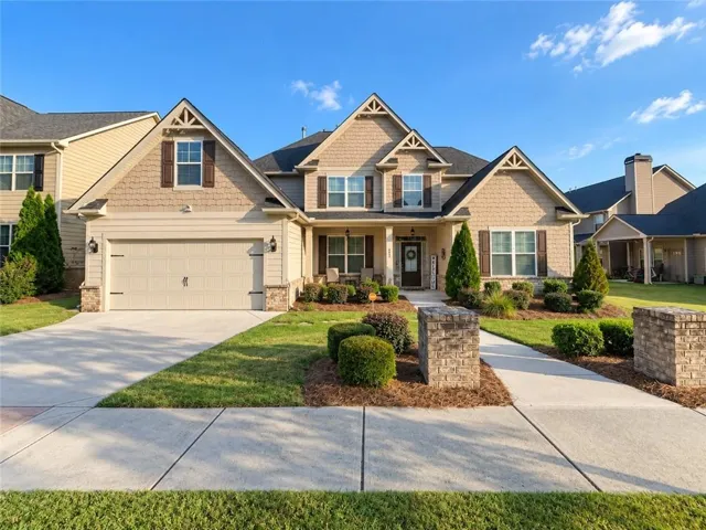 Gabled roofline with decorative trim, stone façade accents, two-car garage, covered front porch, and mature landscaping