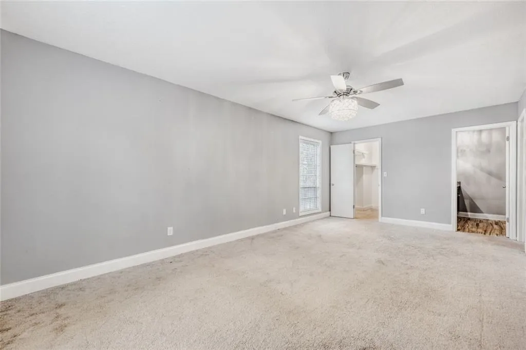 Unfurnished bedroom with a walk in closet, light carpet, and ceiling fan