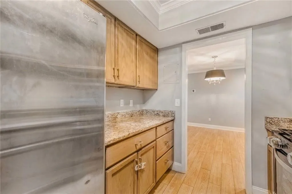Kitchen featuring stainless steel appliances, crown molding, light wood finished floors, light stone countertops, and pendant lighting