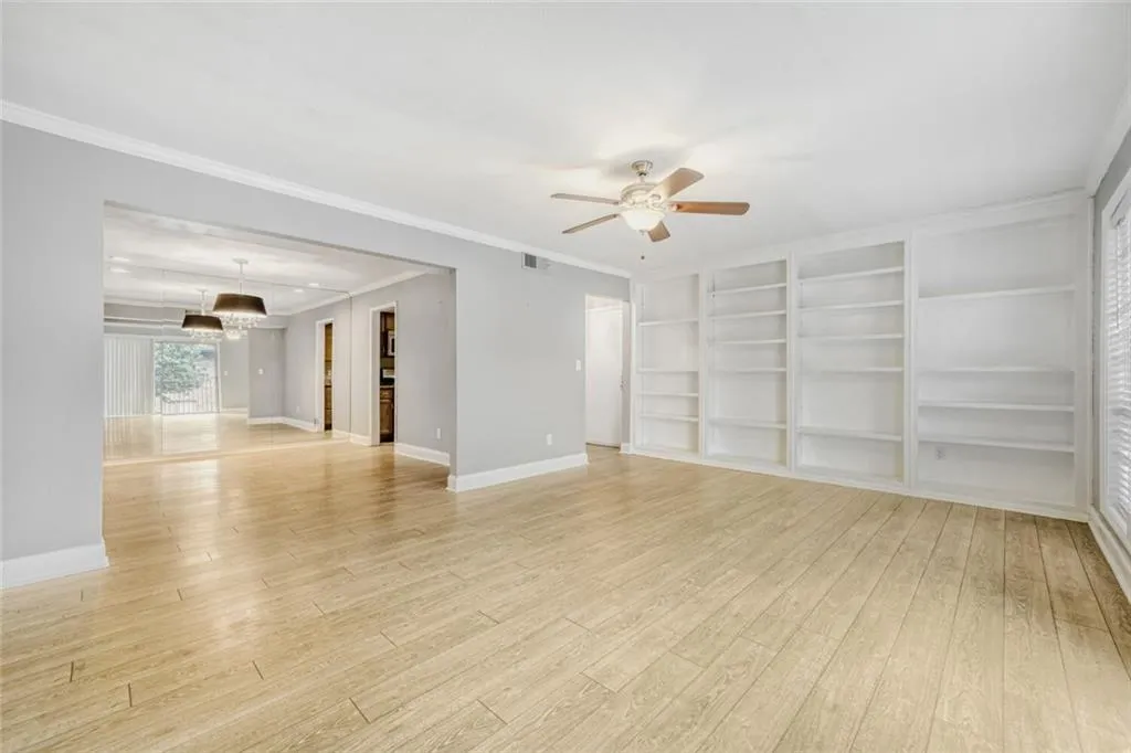 Empty room with a ceiling fan, light wood-style floors, ornamental molding, and built in shelves