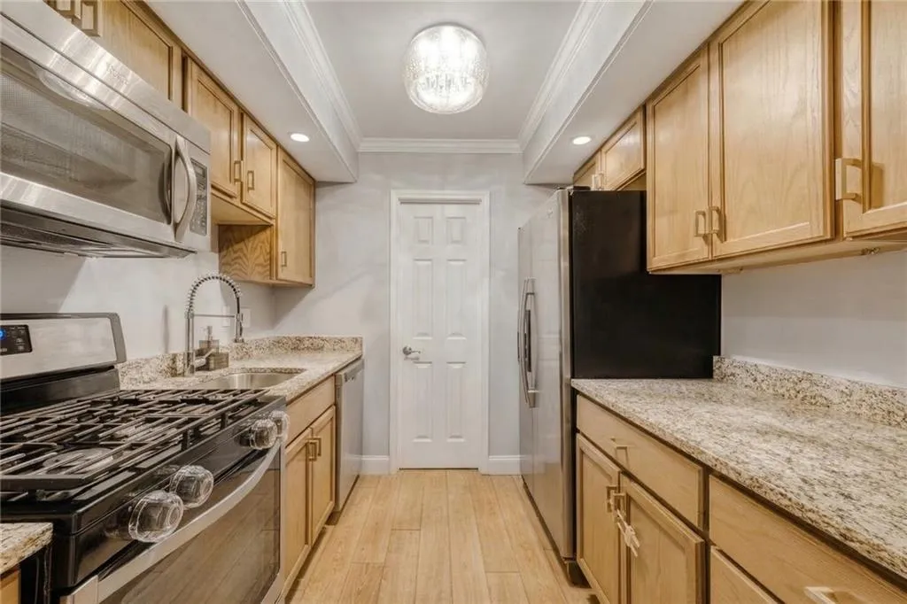 Kitchen with stainless steel appliances, crown molding, light stone counters, recessed lighting, and light wood-style flooring