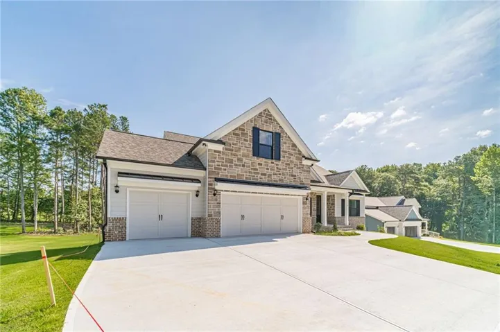 Stone and siding exterior with a multi-car garage, expansive concrete driveway, and a gabled roofline