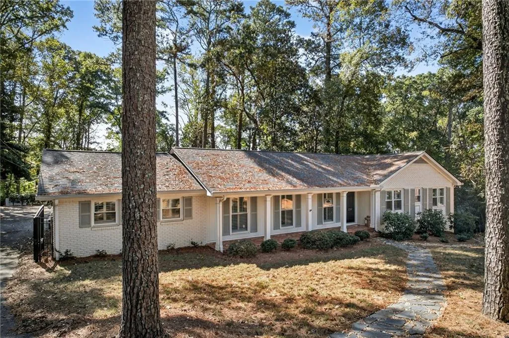 Ranch-style home featuring a porch, brick siding, a front lawn, and view of wooded area