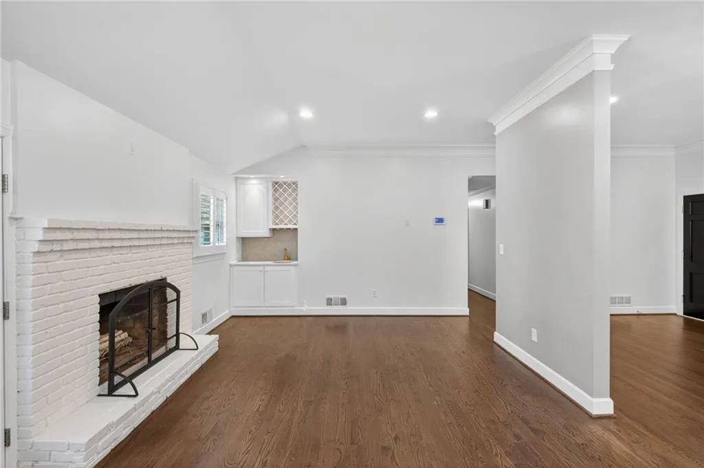 Unfurnished living room featuring a fireplace, dark wood-style floors, vaulted ceiling, recessed lighting, and ornamental molding