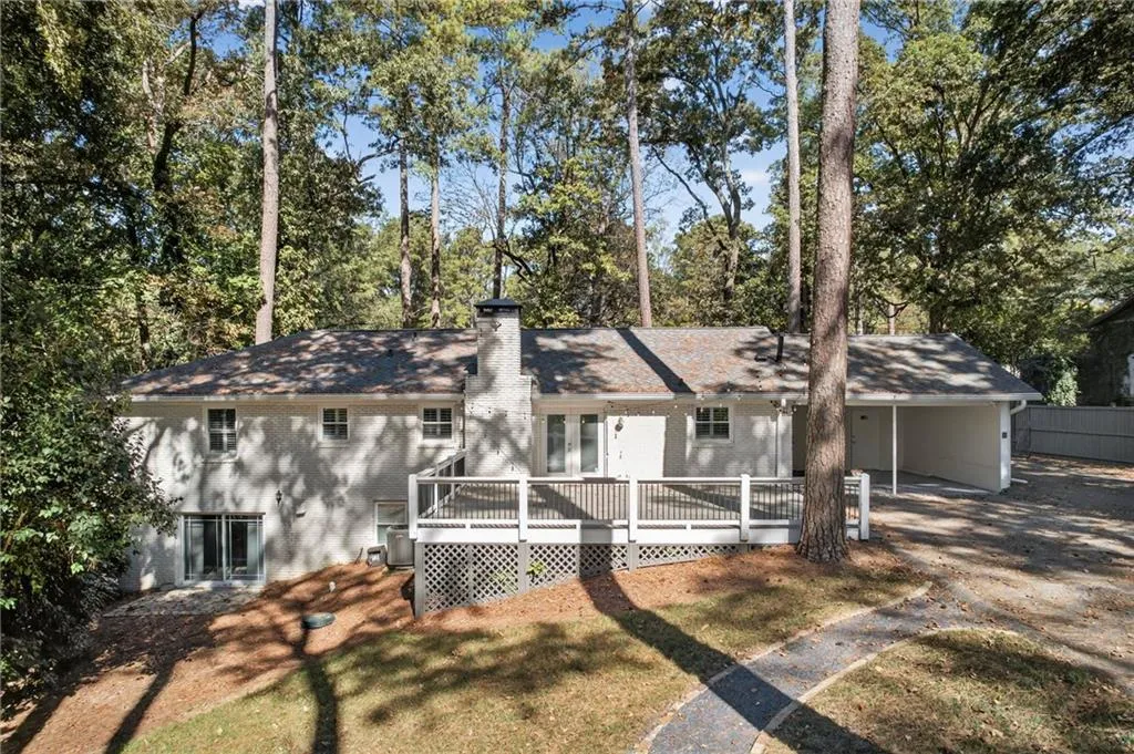 View of front of property with a wooden deck, a carport, a chimney, a front lawn, and driveway