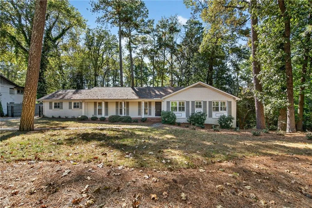 Ranch-style home with view of wooded area, brick siding, and a front lawn