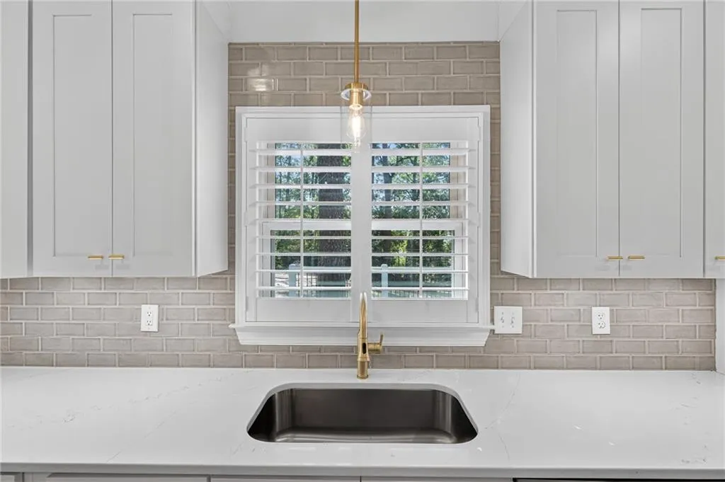 Kitchen view of decorative backsplash, light stone countertops, white cabinetry, and hanging light fixtures