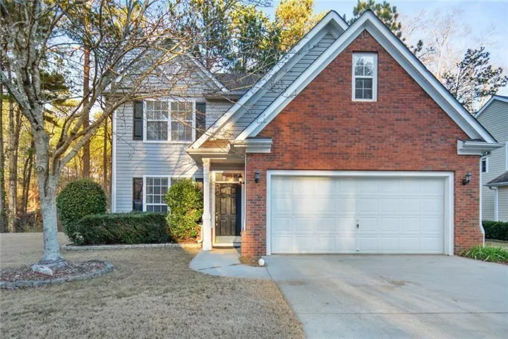 Brick and siding exterior featuring a two-car garage, a covered entry, and mature landscaping