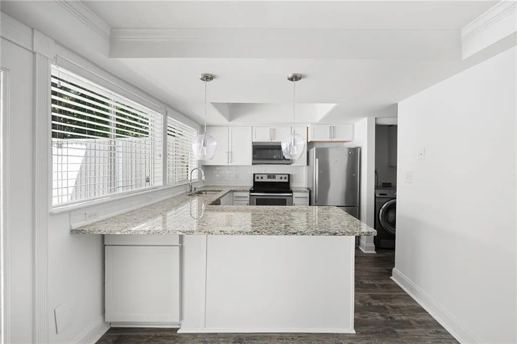 Kitchen with appliances with stainless steel finishes, light stone counters, dark hardwood / wood-style floors, a tray ceiling, and white cabinetry