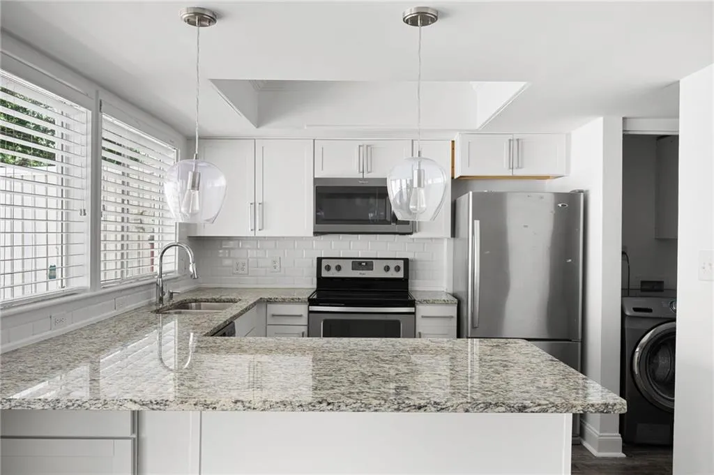 Kitchen featuring backsplash, stainless steel appliances, sink, light stone counters, and washer / dryer