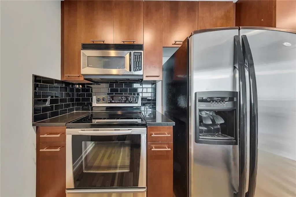 Stainless steel appliances, black subway tile backsplash, wood-finish cabinetry, built-in microwave, and electric range