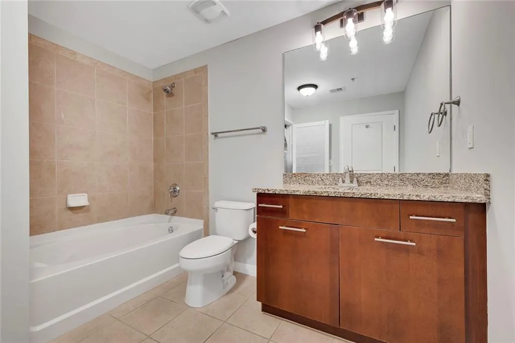 Full-sized bathtub with tiled surround, wood-finish vanity with stone countertop, and large wall-mounted mirror