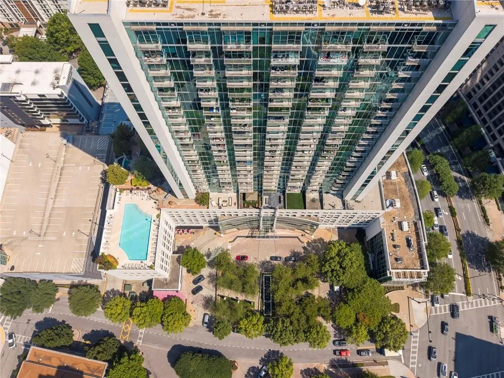 High-rise building with a glass facade, multiple balconies, a ground-level swimming pool, an adjacent parking structure, and surrounding street access