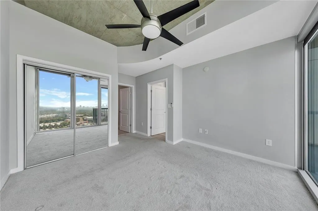 Carpeted flooring, mirrored sliding closet doors, concrete ceiling, ceiling fan, and full-height windows