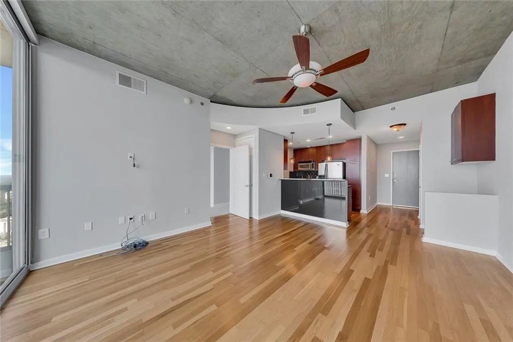 Hardwood flooring throughout, exposed concrete ceiling, full-height glass sliding doors, ceiling fan with light fixture, and kitchen with dark wood cabinetry
