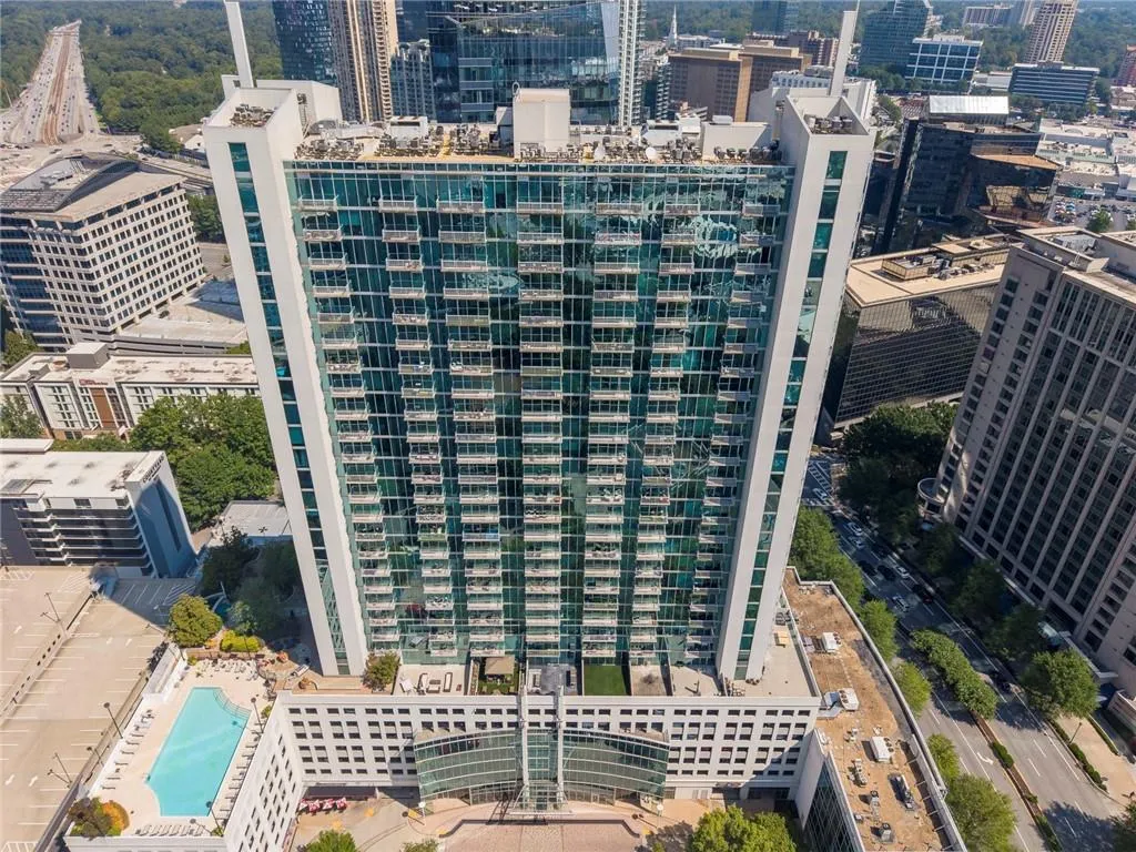 High-rise building featuring a glass facade, multiple balconies, a rooftop deck, and an adjacent outdoor swimming pool
