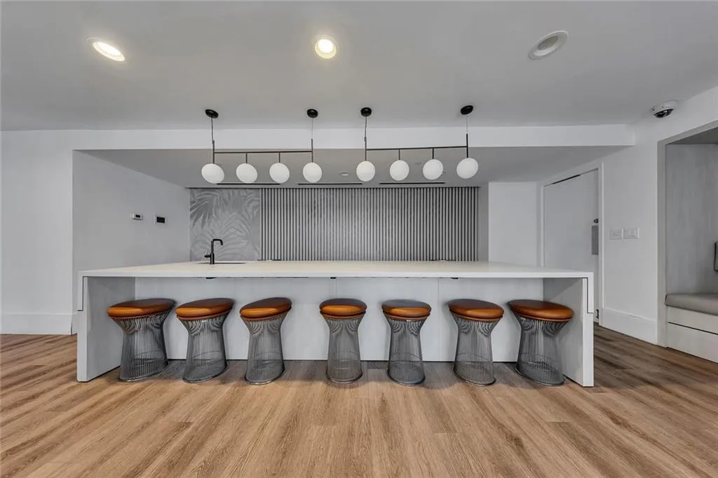 Extended island with integrated sink and matte black faucet, linear pendant lighting, recessed ceiling lights, and wood-finish flooring
