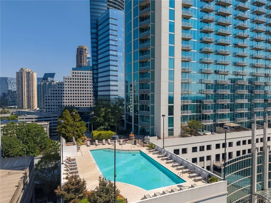 Rooftop swimming pool with surrounding lounge deck, bordered by established landscaping, and high-rise building architecture