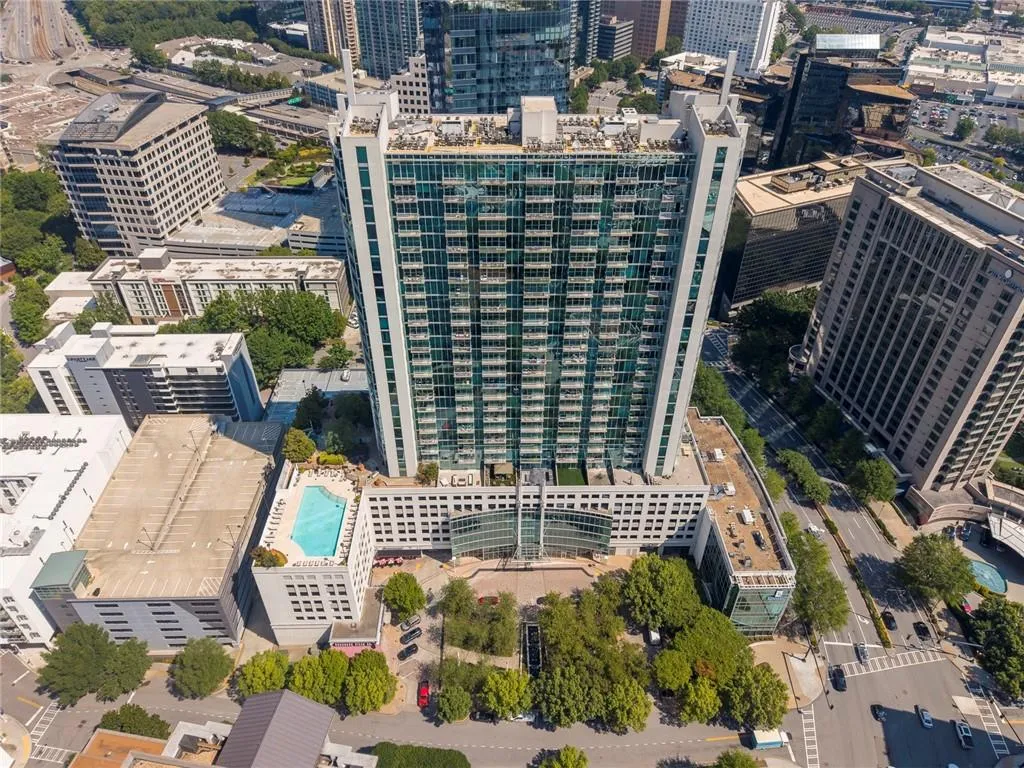 Modern high-rise residential building with a multi-story base, featuring a rooftop swimming pool and integrated street-level landscaping