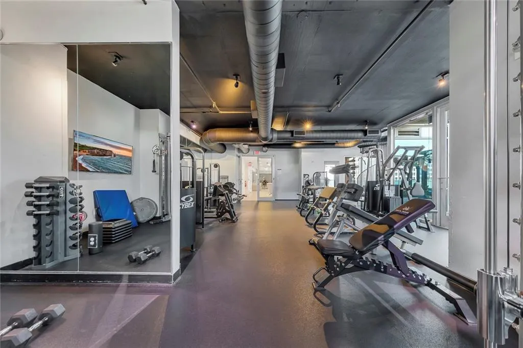 Fitness center featuring exposed ductwork, track lighting, full-height mirrored wall, and floor-to-ceiling windows