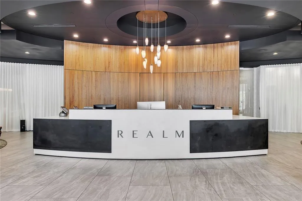 Curved reception desk with integrated branding, wood-paneled feature wall, suspended light fixture, recessed ceiling lighting, and tiled flooring