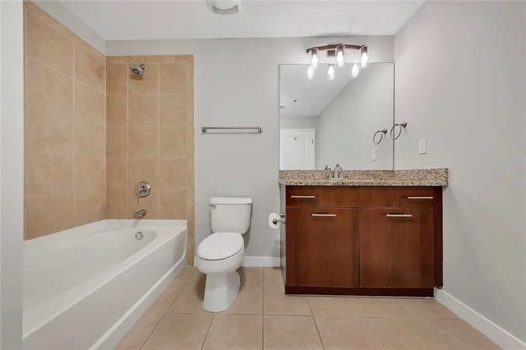 Full-sized bathtub with tiled surround, wood-finish vanity with countertop, and large vanity mirror with overhead lighting