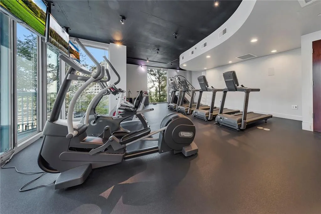 Fitness center featuring full-height windows, a curved architectural ceiling element, recessed lighting, and resilient flooring