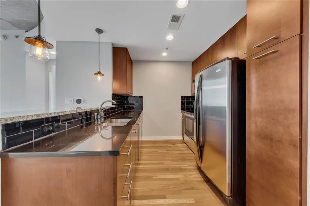 Kitchen featuring wood-finish flooring, stainless steel appliances, dark subway tile backsplash, sleek countertops, and rich wood-tone cabinetry
