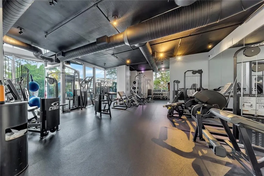 Fitness center featuring an exposed duct system, track lighting, expansive windows, and rubber flooring